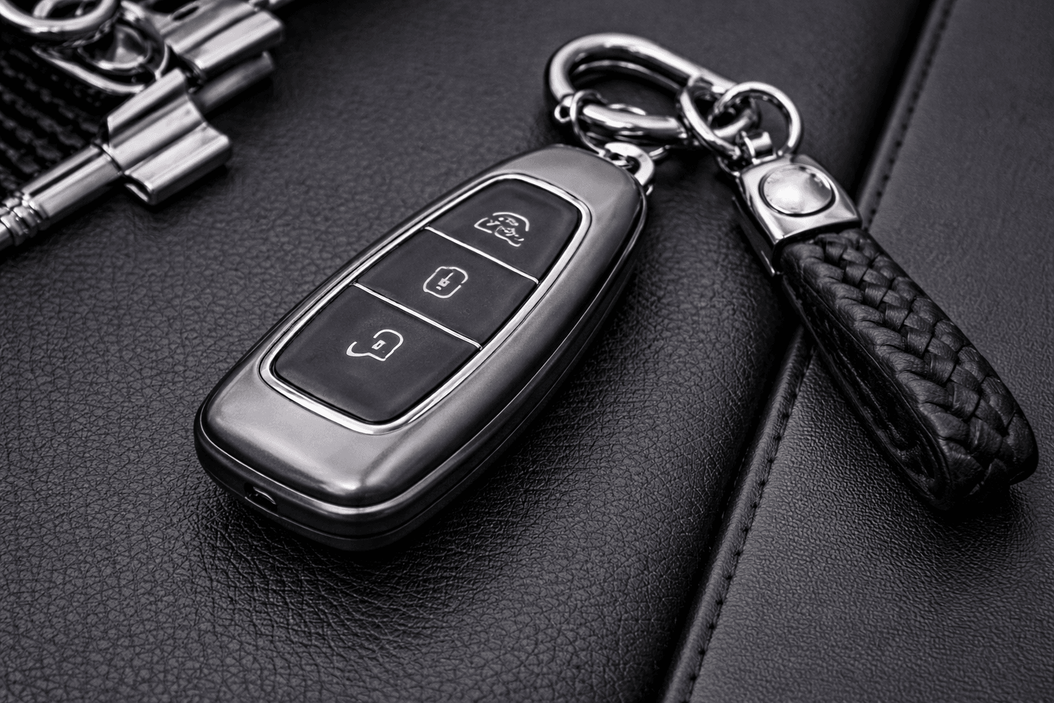 Car key fob in a protective case with a braided leather keychain on a dark leather surface