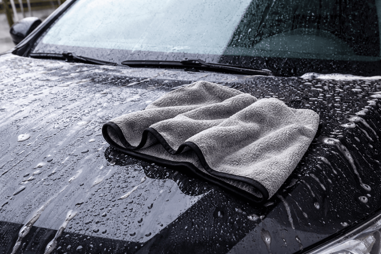 Grey microfibre drying towel folded on a wet black car bonnet