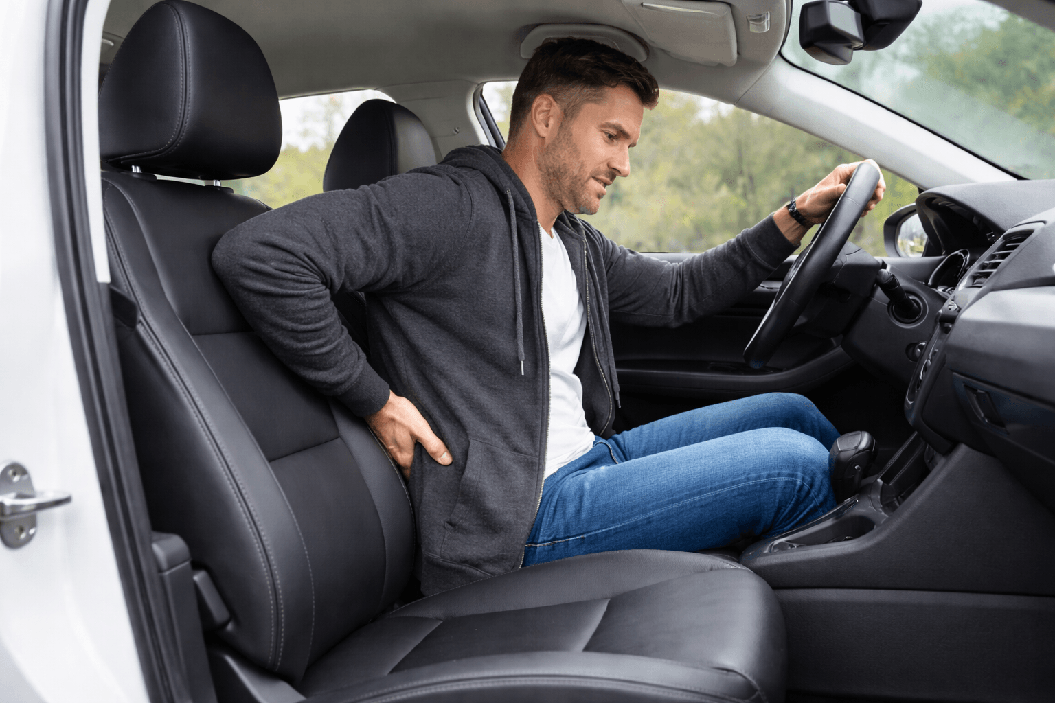 Man holding his lower back in discomfort while driving, before using a lumbar support cushion
