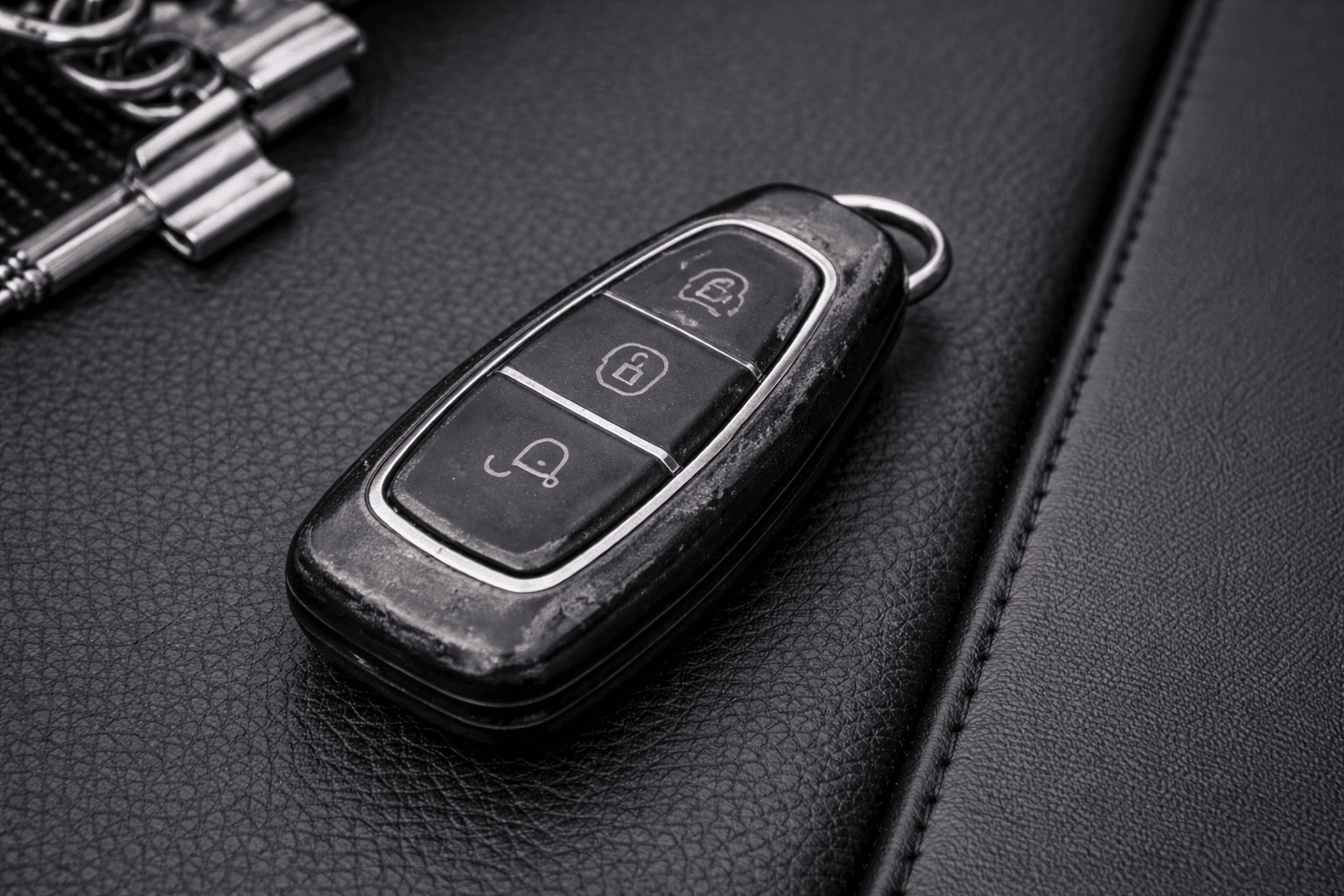 Worn, scratched bare car key fob on a black leather surface, before fitting a protective case